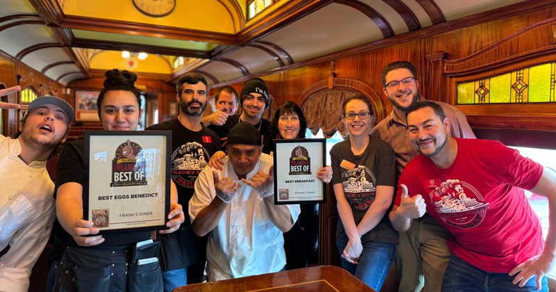 Smiling staff pose inside, two members hold awards for Best Eggs Benedict and Best Breakfast