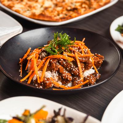 Ginger beef dish on a table with other food plates.