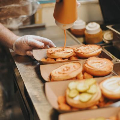 Chef adding a sauce to several chicken sandwiches on a metal prep counter.