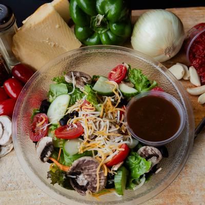 Mixed greens salad with mushrooms, cucumbers, cheese, tomatoes, and dressing.