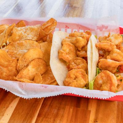 Shrimp tacos with chips on a wooden table.