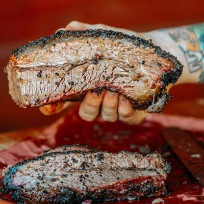 A hand holding a piece of smoked brisket.
