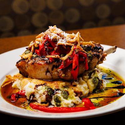 Grilled pork chop on mashed potatoes with red peppers and cheese.