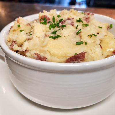 Shepherd’s pie with rustic mashed potatoes and chopped chives in a white crock..