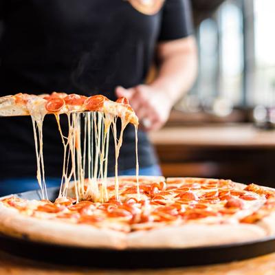 Hands grabbing a slice of the pepperoni pizza.