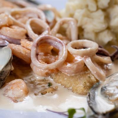 Close-up view of shrimp, calamari, and mussels in a white sauce.