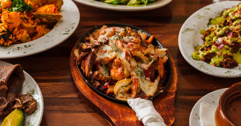 Mixed fajita surrounded by various other food dishes on a wooden table