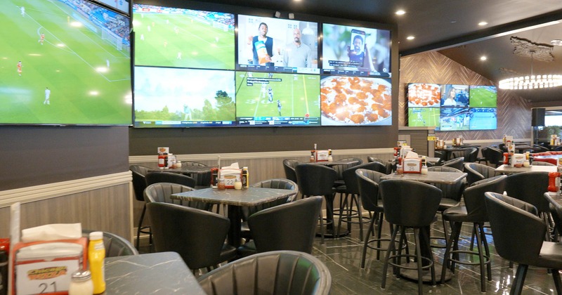 Interior, tables and chairs with tv screens on the wall behind