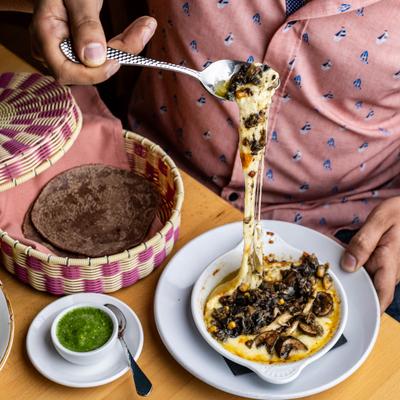 A person pulling stretchy melted cheese with mushrooms from a hot skillet.