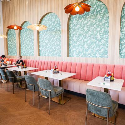 Interior,  a long pink tufted banquette with square marble-top tables and gray upholstered chairs.