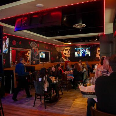 A lively restaurant features vibrant Day of the Dead-themed murals, guests dining.