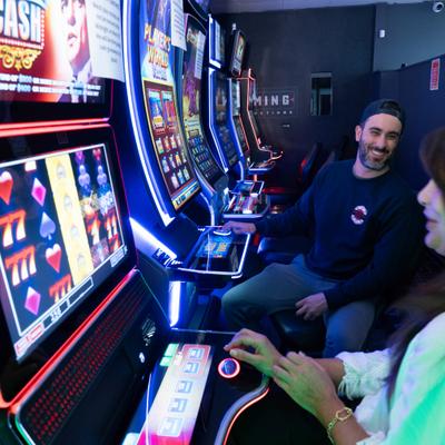 Two people laughing and playing slot machines together.