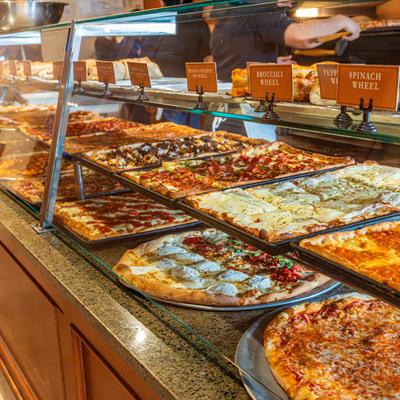 Glass display case with assorted pizzas labeled with names.