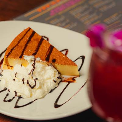Vanilla flan cake with whipped cream and chocolate drizzle on a white plate.