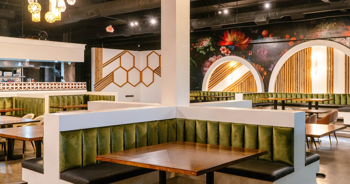 A modern  interior - green velvet cushioned booths, wooden tables, pendant lights, a floral mural