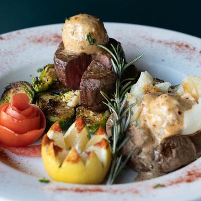 Seared beef, roasted brussels sprouts,  baked potato, vegetable garnish and rosemary sprig.