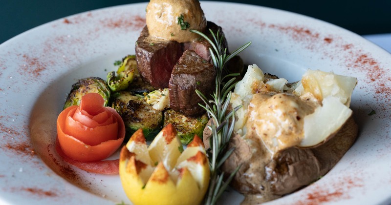 Seared beef, baked potato, roasted brussels sprouts, vegetable garnishes and rosemary sprig