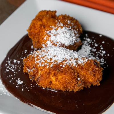 Fried dessert pieces dusted with powdered sugar, atop chocolate sauce on a white plate.