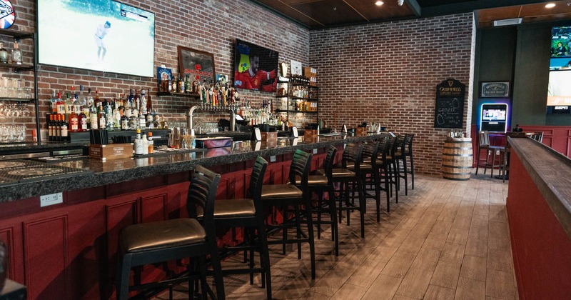 Interior featuring a bar with chairs, TVs, and bottles of hard liquor