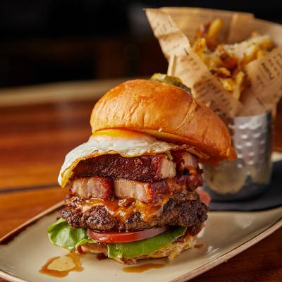 Cheeseburger with pork belly, sunny egg, and a side of fries.