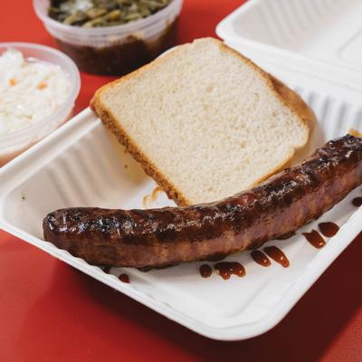 Grilled sausage with a slice of white bread and sides.