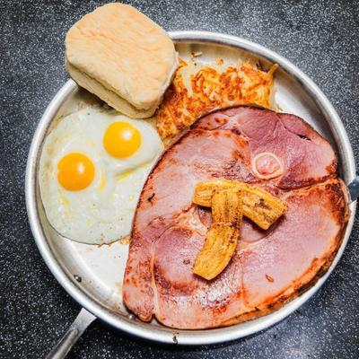 Breakfast skillet with ham steak, eggs, hash browns, and biscuit.