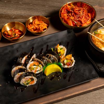 Platter with sushi rolls, fishcake soup, kimchi and dipping sauces.