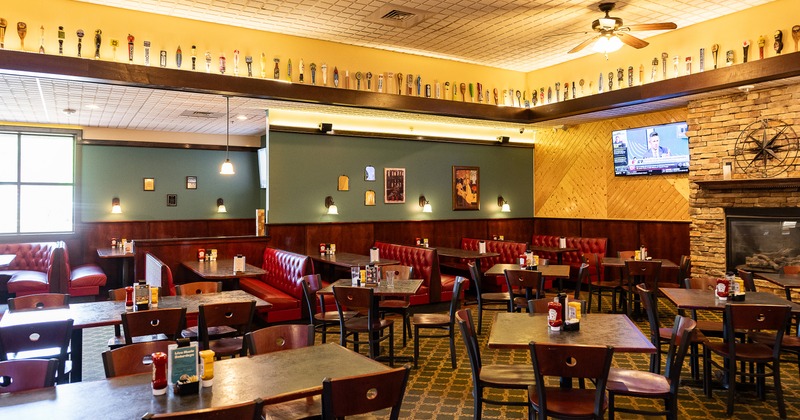 Cozy dining area with a fireplace, tables, chairs, and upholstered booths along the wall