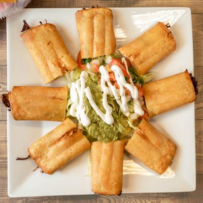 Plate of flutas with guacamole and pico de gallo in the middle.