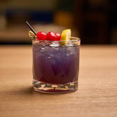 Purple rain cocktail, garnished with cherries and lemon slice.