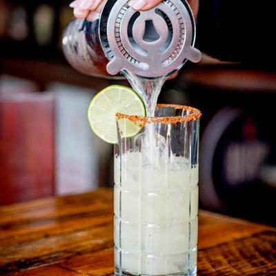 Spicy jalapeno margarita being poured into a glass on a table.