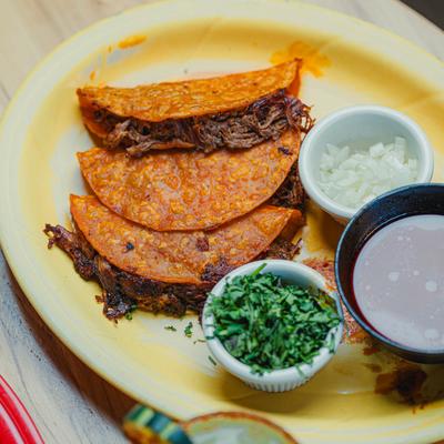 Quesabirria tacos served with dipping broth, cilantro, and onions.