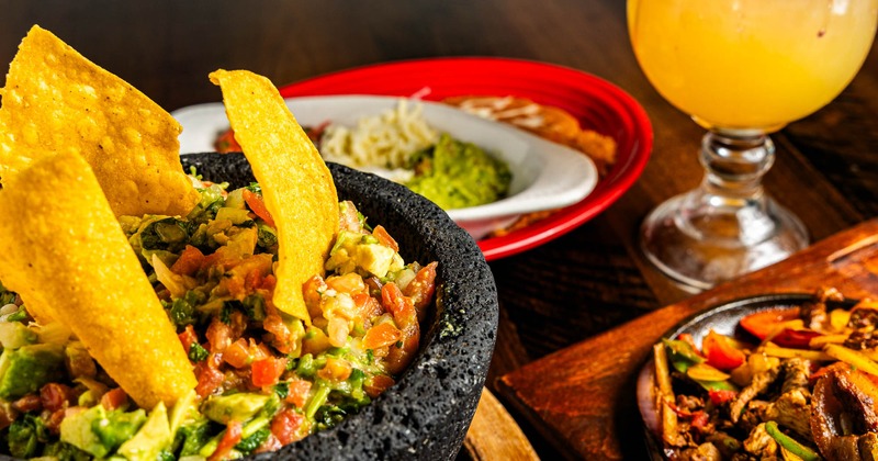 Guacamole dip and chips on a table with assorted dishes and Margarita drink