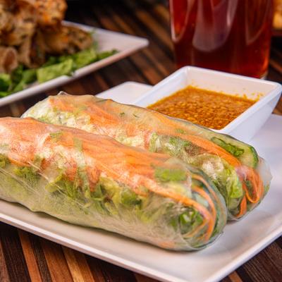 Two fresh spring rolls with vegetables and peanut dipping sauce on a white plate.