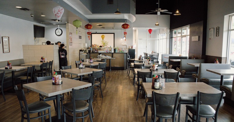 Interior of an Asian themed restaurant with wooden flooring, tables, chairs, hanging lanterns, and large windows