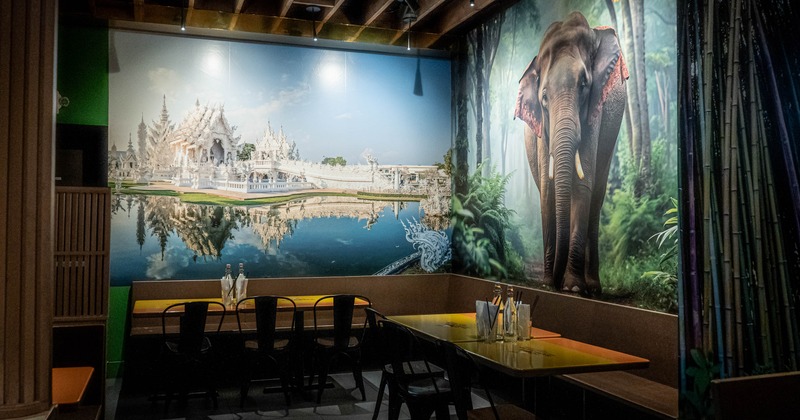 Interior with tables and metal chairs; a large mural of a temple and an elephant on the walls