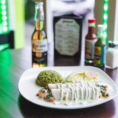 A plate of enchiladas margaritas served on a dining table with a bottle of beer.