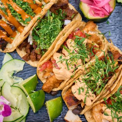 Assorted tacos served on a black plate with garnishes.