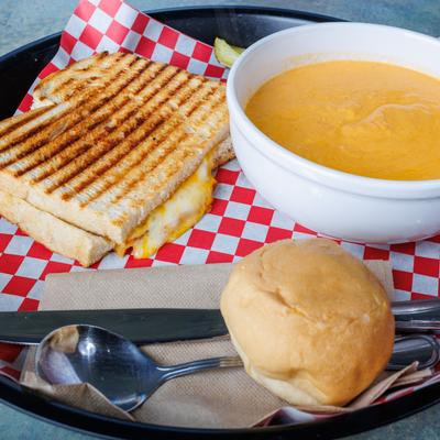 Grilled cheese sandwich served with lobster bisque soup and a bread roll.