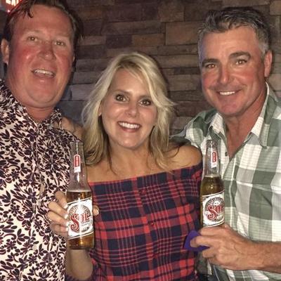 Interior, three people holding beers and smiling while posing together for a shot.