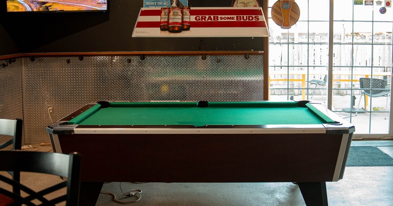 Green felt pool table in a bar with beer advertisements and television