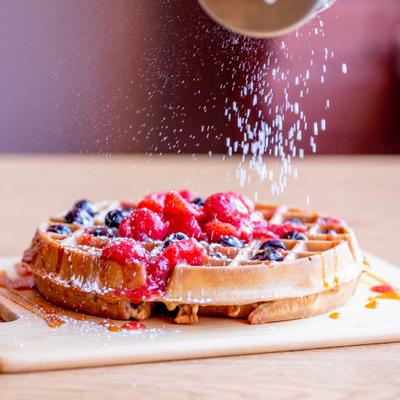 Waffle topped with fresh berries and powdered sugar being sprinkled on top.