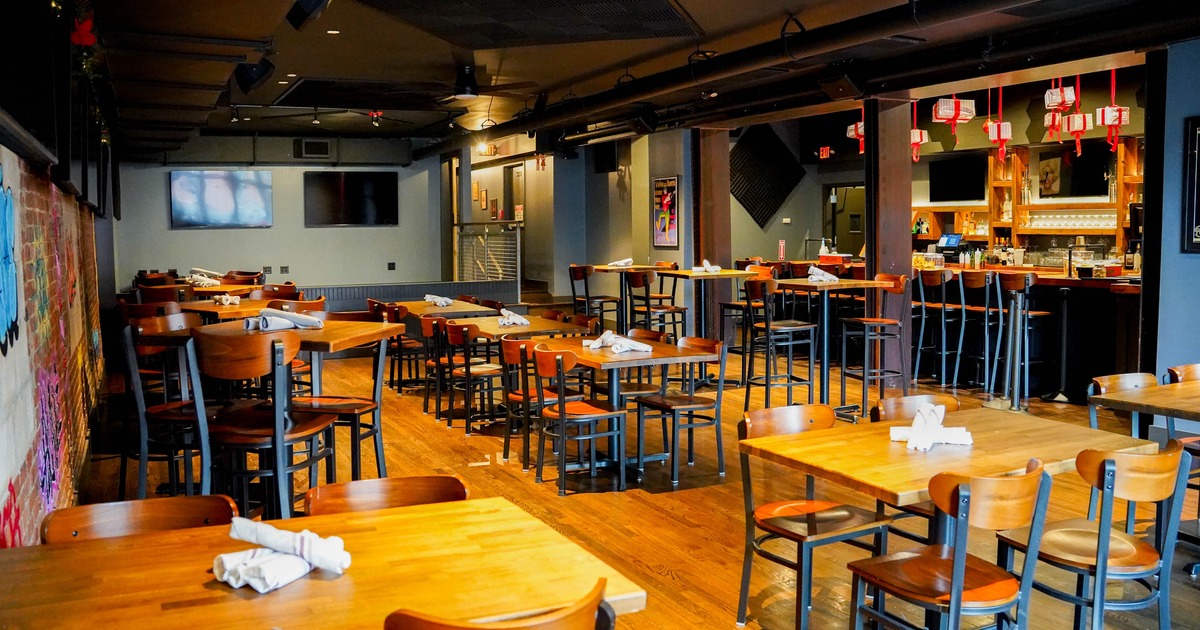 Interior of a restaurant with wooden floors, tables and chairs, a bar area, and modern lighting
