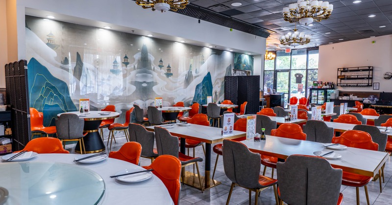 A modern restaurant interior with orange and gray chairs, white tables, mural on the wall