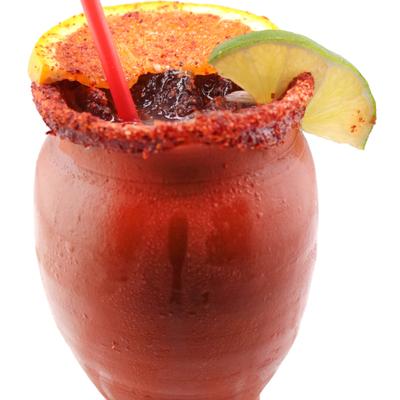 Cocktail served in a chili-rimmed clay cup, garnished with citrus slices.