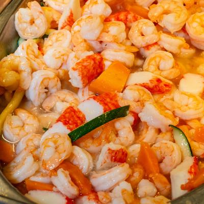 A buffet tray filled with cooked shrimp, imitation crab meat, zucchini, and sliced carrots.
