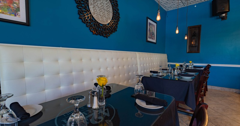An upscale interior with blue walls, white tufted bench and elegantly set tables