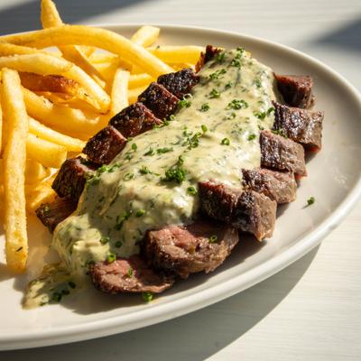 Sliced steak topped with a creamy, herb-infused sauce, served with fries.