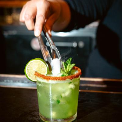 A bartender adds ice to a refreshing green margarita with lime, mint, and spicy rim.