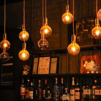 Hanging light bulbs above the bar with shelves with various bottles in the background.